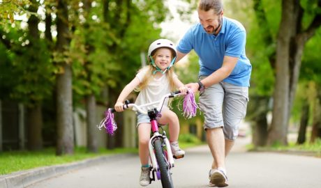 Una nena aprenent a anar en bicicleta amb l'ajut d'un adult (iStock)