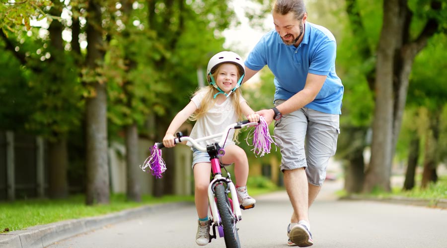 Una nena aprenent a anar en bicicleta amb l'ajut d'un adult (iStock)