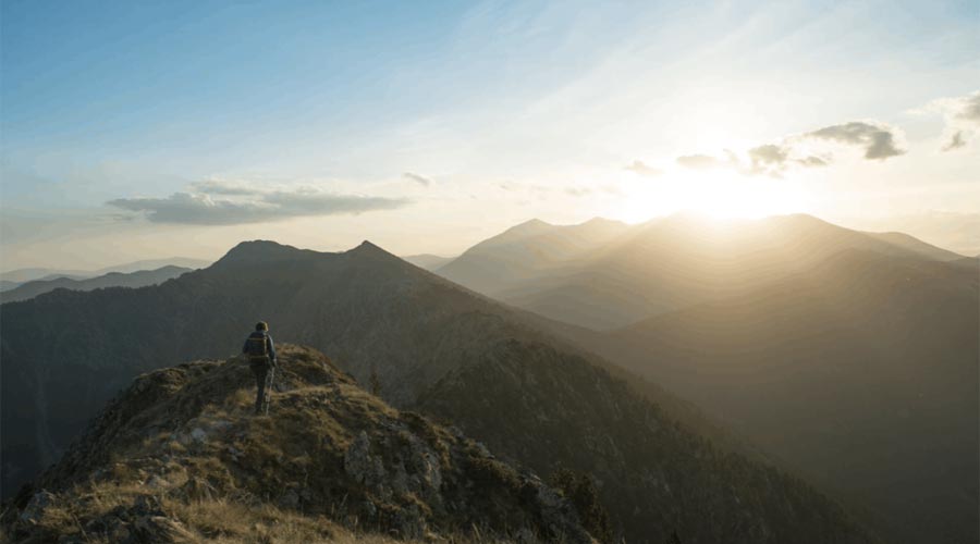 Home passejant per la muntanya amb el sol al davant