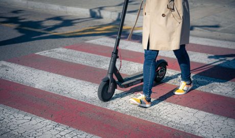 Una persona passant per un pas de vianants amb un patinet sense conduir-lo