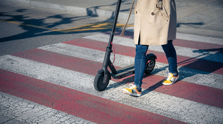 Una persona passant per un pas de vianants amb un patinet sense conduir-lo (Gencat.cat)