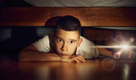 Un noi amagat sota del llit amb una llanterna