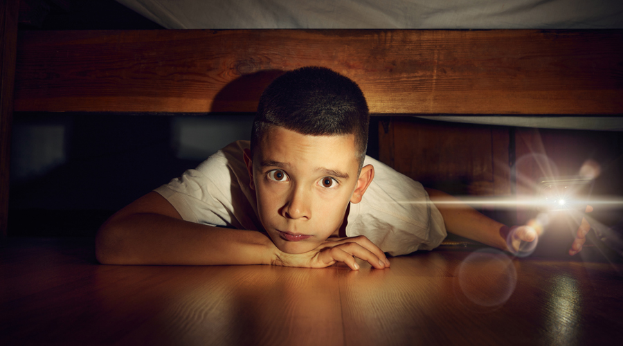 Un noi amagat sota del llit amb una llanterna (Getty Images)